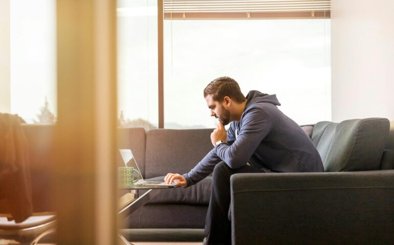 Ein Mann der auf einem Sofa vor seinem Laptop sitzt.